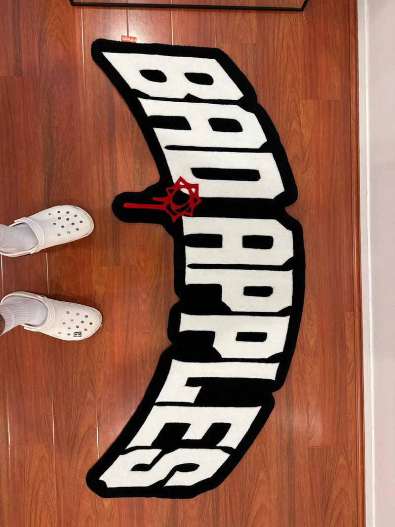 Handmade tufted rug with 'Bad Apples' text in bold black and white on wooden floor