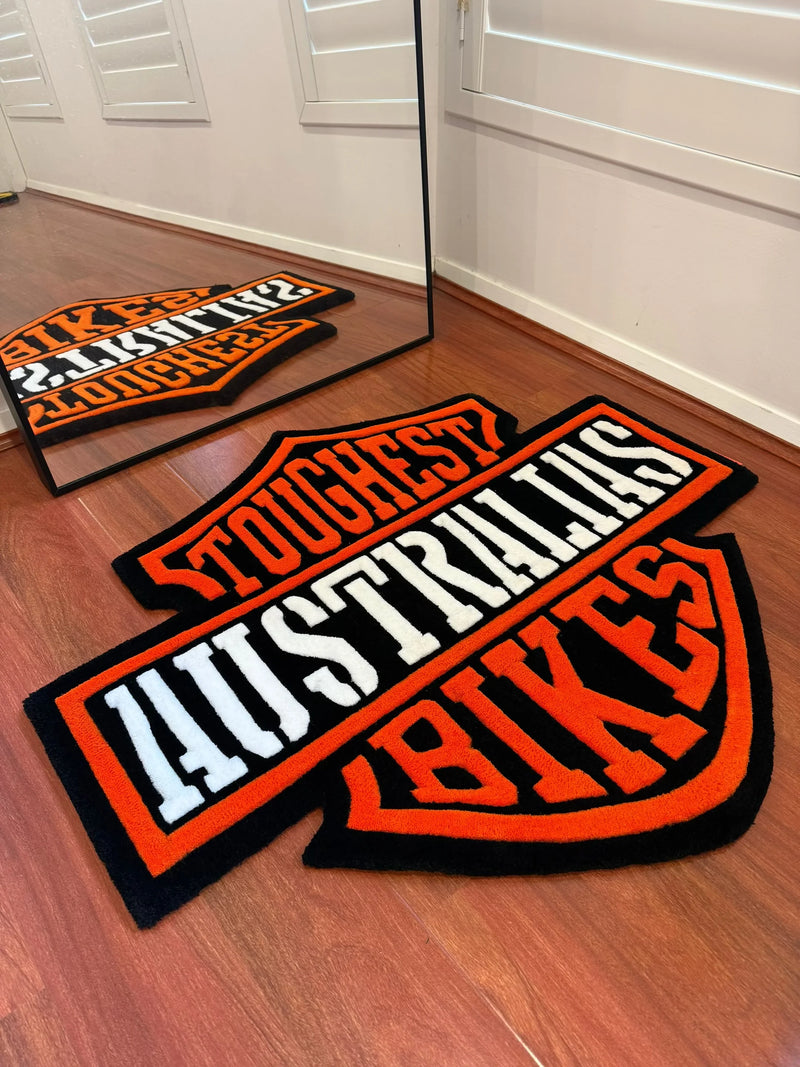 Handmade tufted rug with 'TOUGHEST AUSTRALIAN BIKES' text in black, orange, and white on wood floor