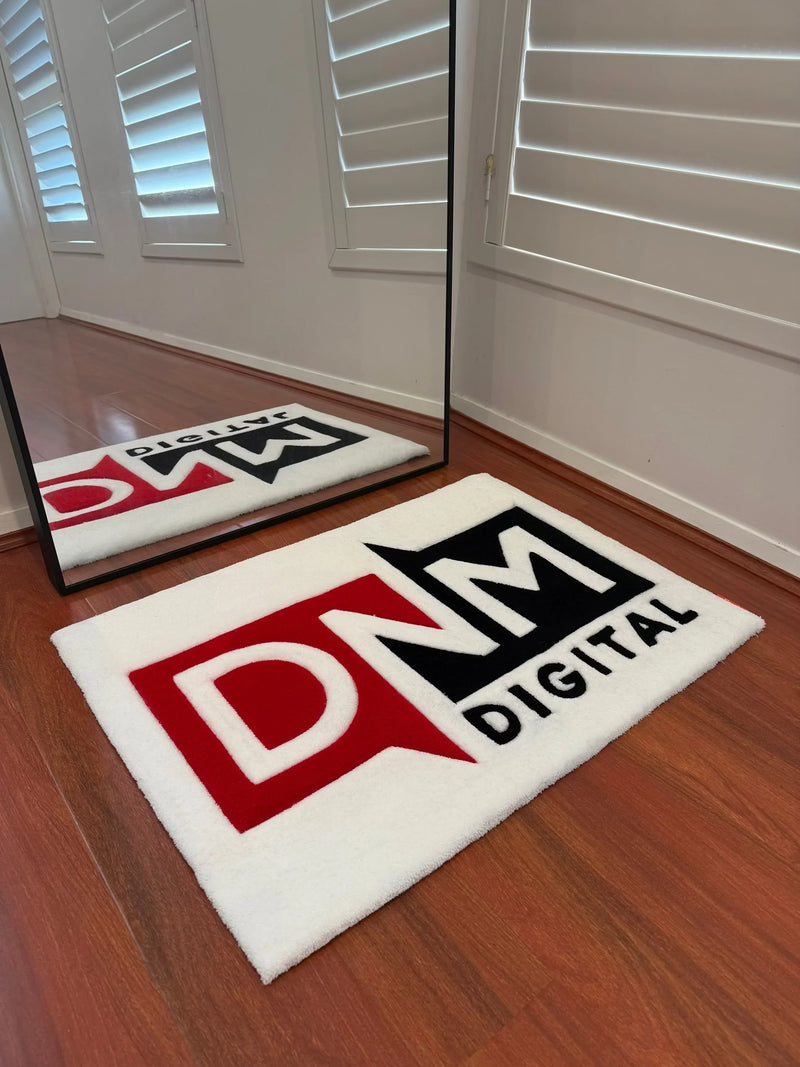 Handmade tufted custom rug with 'DNM DIGITAL' logo on white background, on wooden floor.