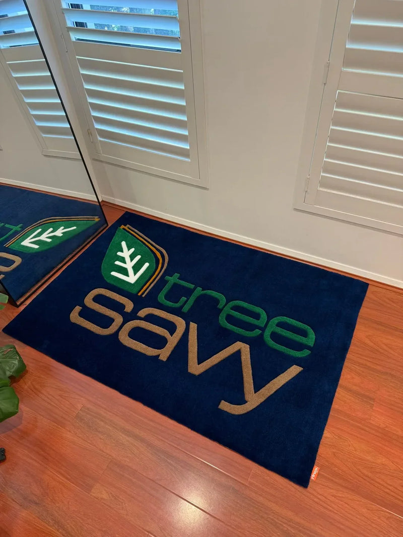 Handmade tufted rug with 'tree savy' logo, blue background, on wooden floor by window