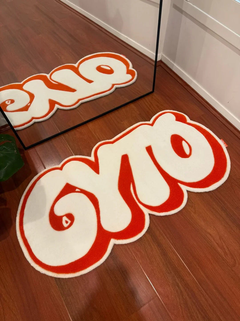 Handmade tufted rug with bold white and red 'gyro' text, on wooden floor by mirror.