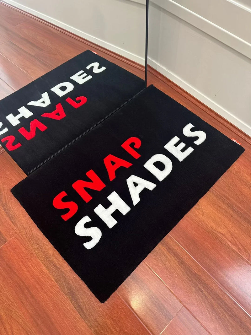 Handmade black tufted rug with red and white 'SNAP SHADES' text on wooden floor