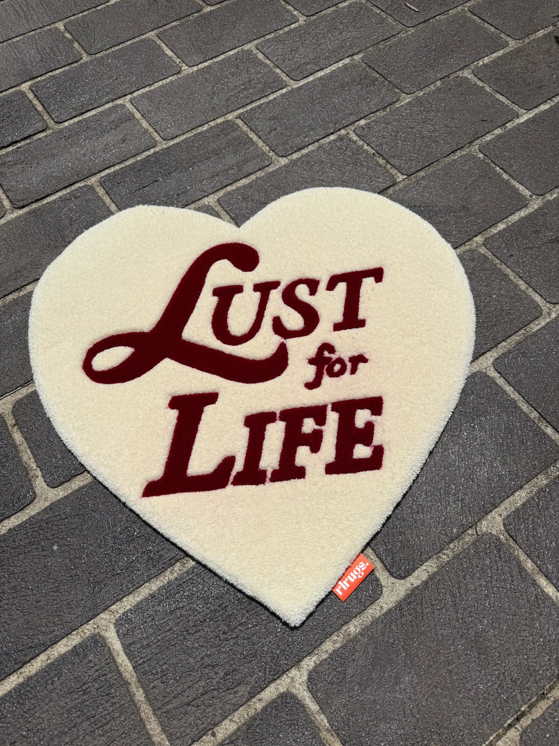 Heart-shaped cream handmade tufted rug with 'Lust for Life' text on brick pavement