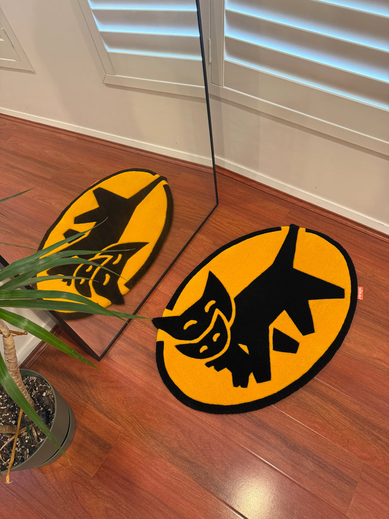 Handmade tufted rug with black cartoon cat design on yellow oval, on wooden floor near mirror.