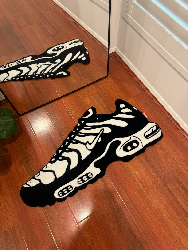 Handmade black and white sneaker-shaped tufted rug on wooden floor near mirror