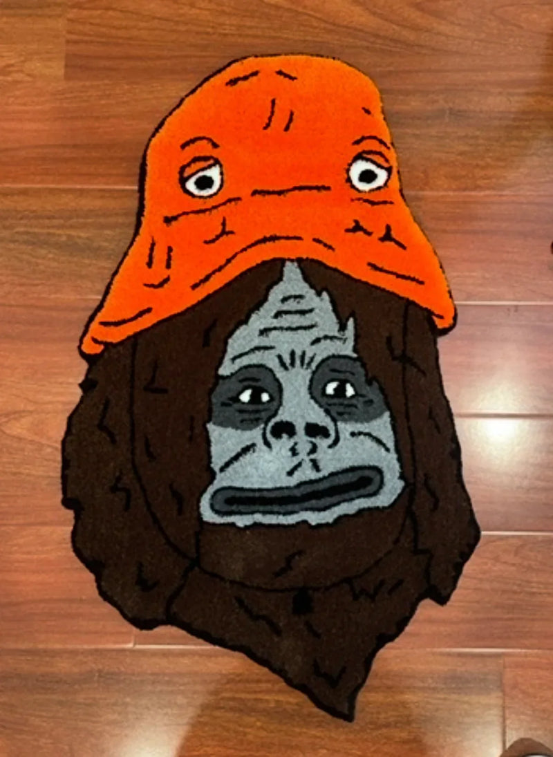 Handmade tufted rug featuring a grey gorilla face with an orange hat, on wooden floor.