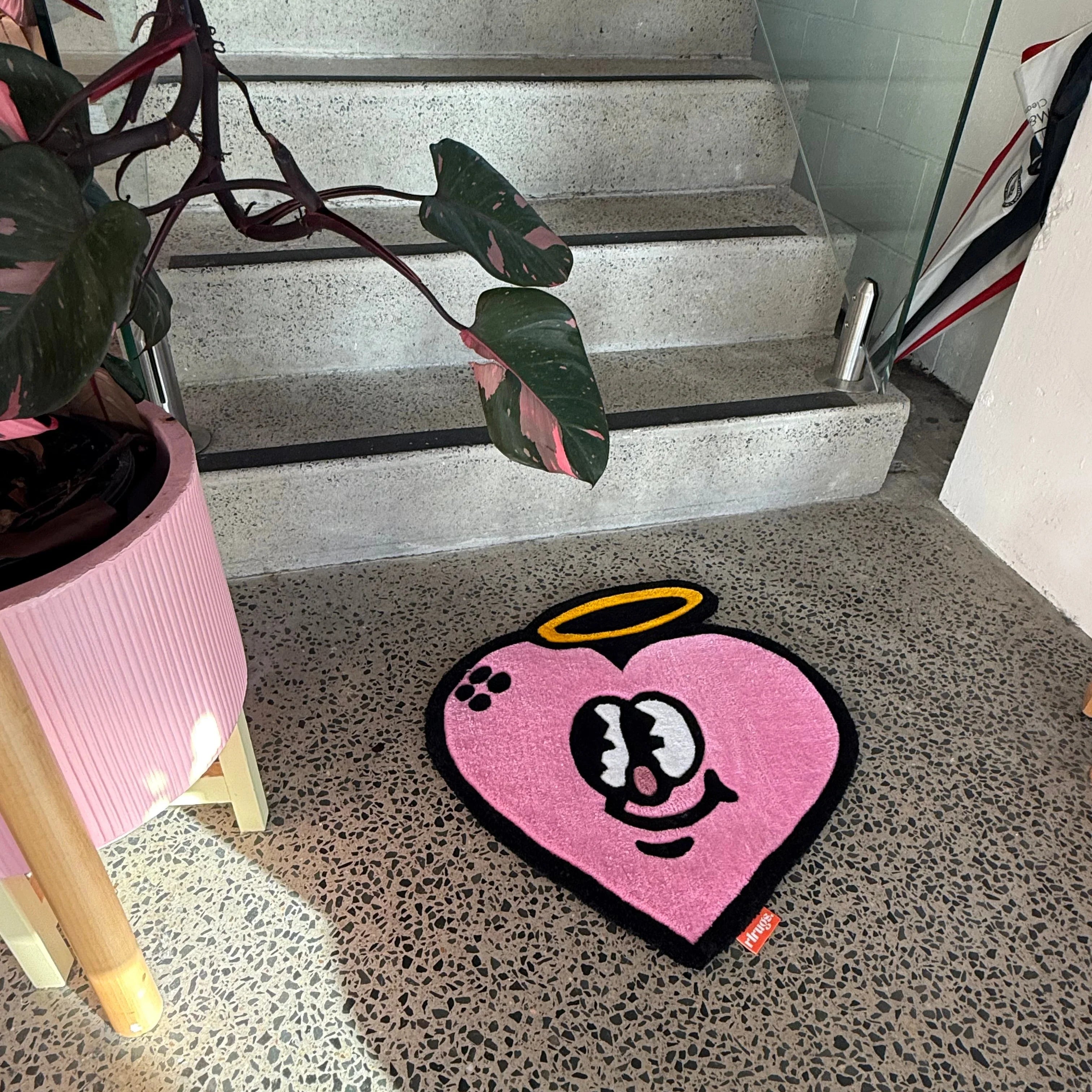 Handmade pink heart-shaped rug with cartoon face and halo on terrazzo floor near stairs