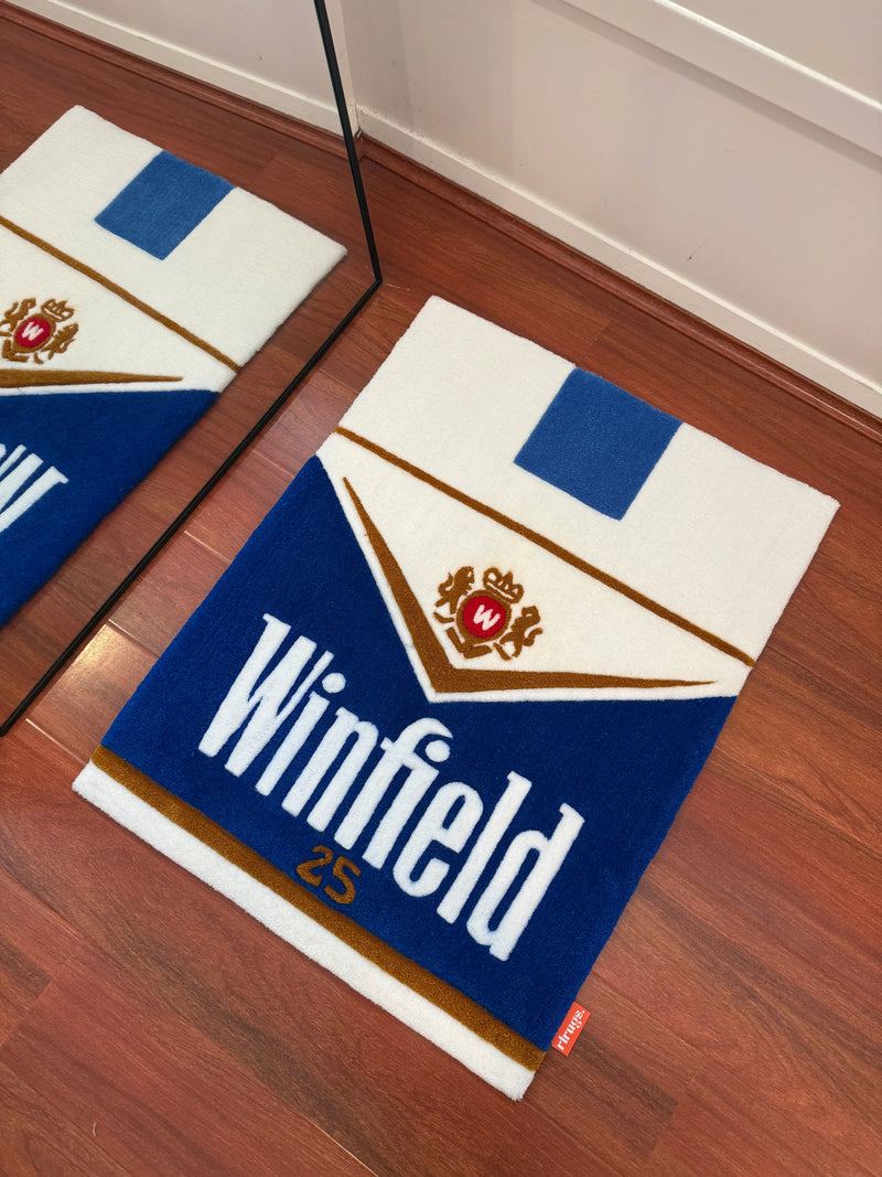 Handmade tufted rug with blue, white, and gold design and 'Winfield 25' text on wooden floor