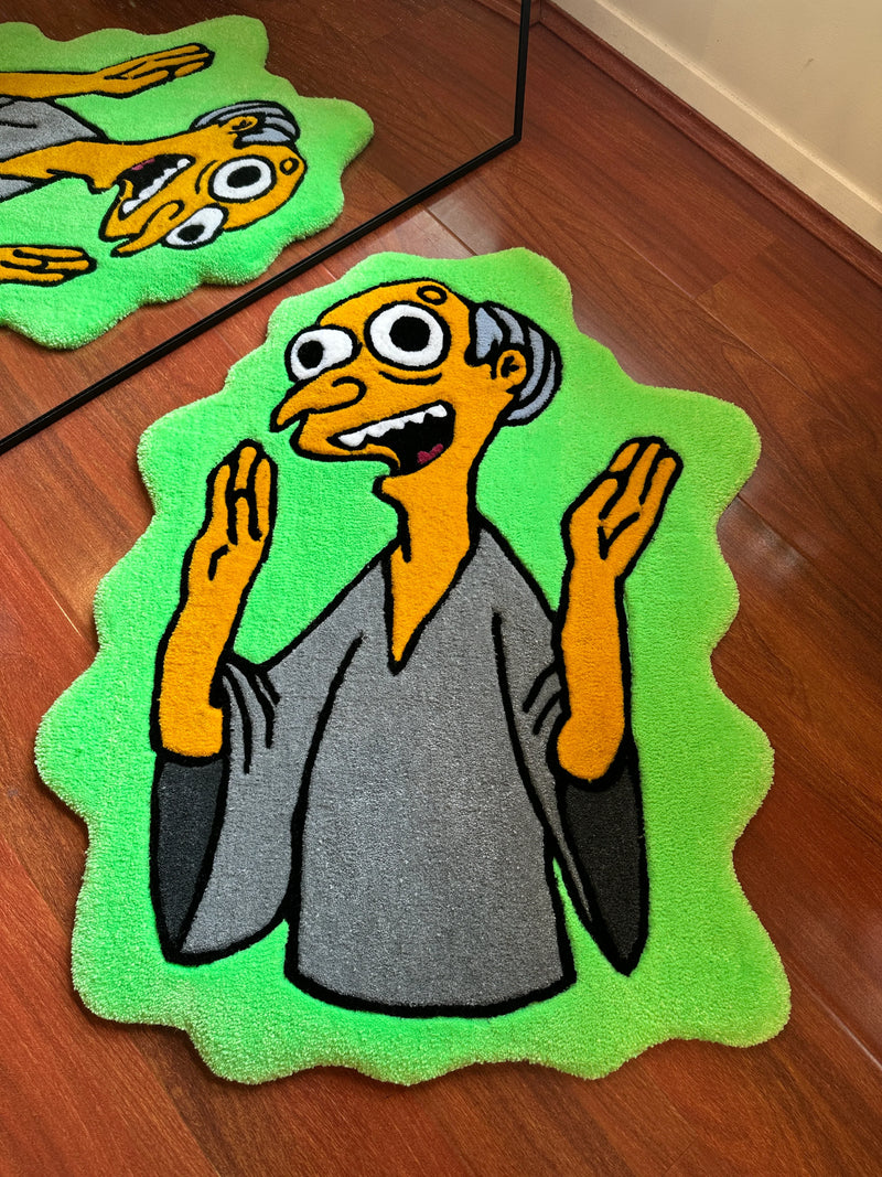 Handmade tufted rug with cartoon character design on green background, displayed on wood floor