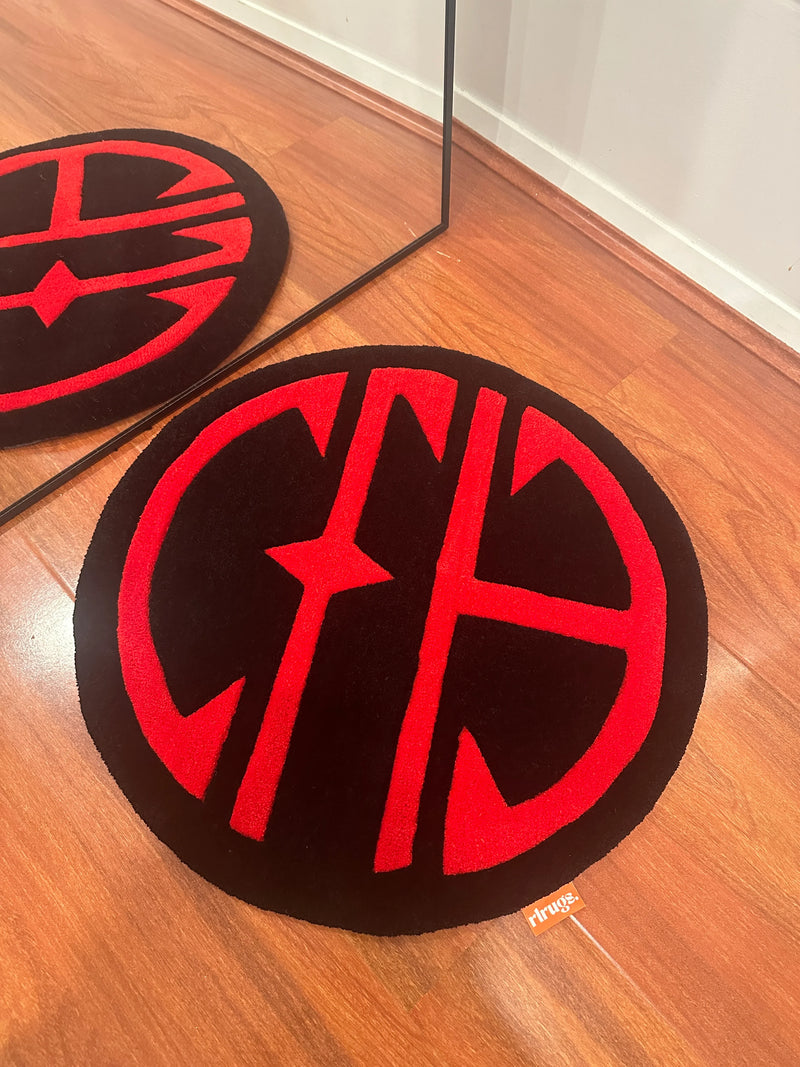 Round handmade tufted rug with bold red geometric pattern on black, reflected in mirror