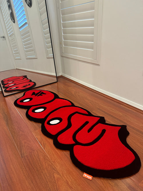 Handmade red and black tufted rug with playful cartoon design on wooden floor by a mirror