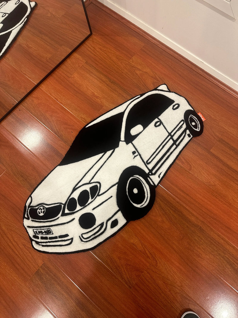Handmade tufted rug shaped like a black and white cartoon car on wooden floor