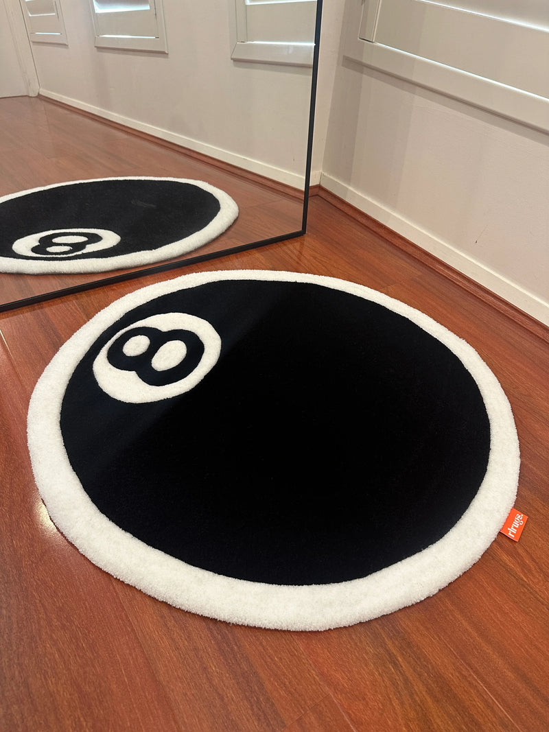 Round black and white tufted rug resembling an 8-ball on wooden floor near a mirror