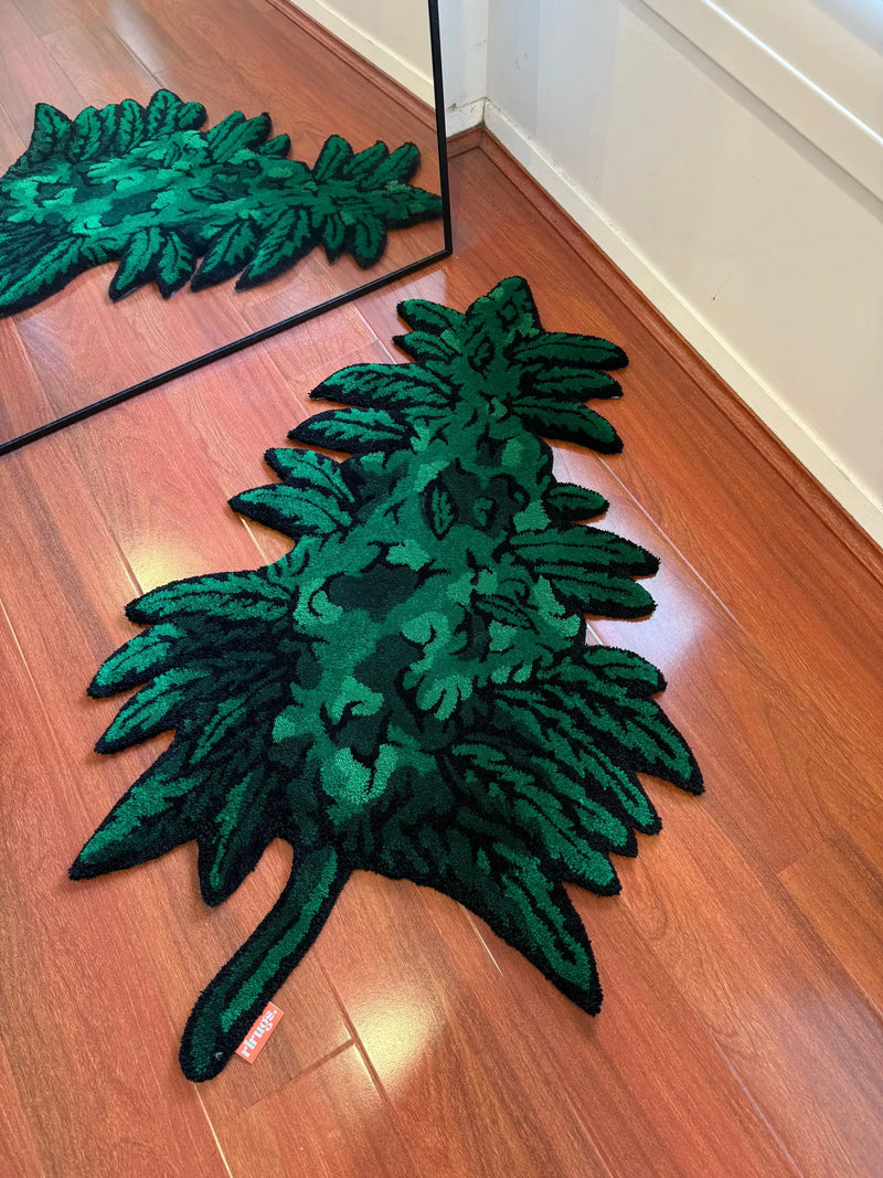 Handmade green leaf-shaped tufted rug on wooden floor, reflected in a mirror.
