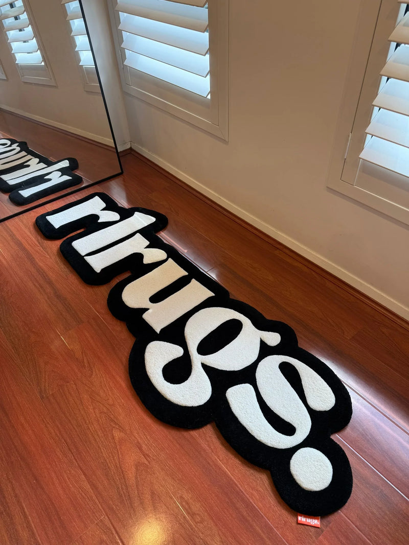 Handmade tufted black and white rug with bold text on wooden floor near window shutters