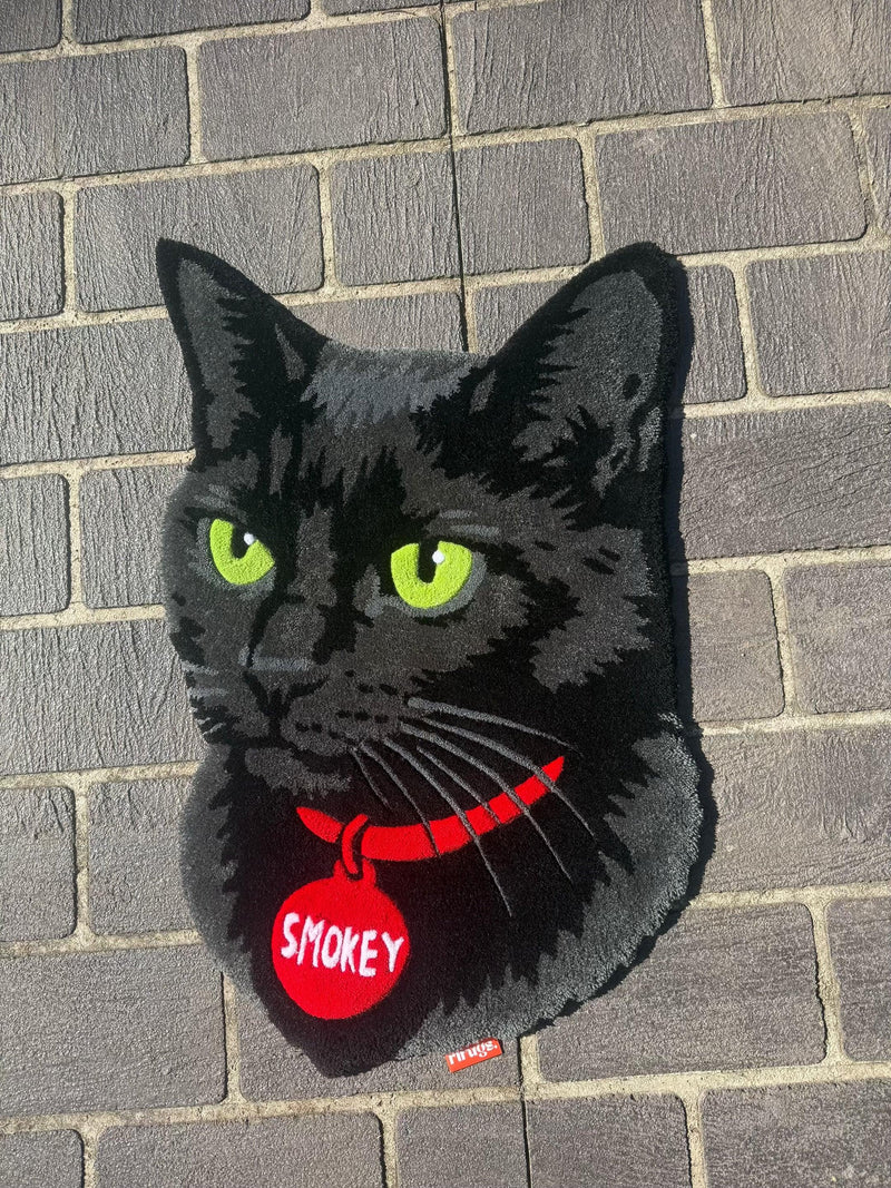 Handmade tufted rug of a black cat with green eyes, red collar, and Smokey tag on brick wall