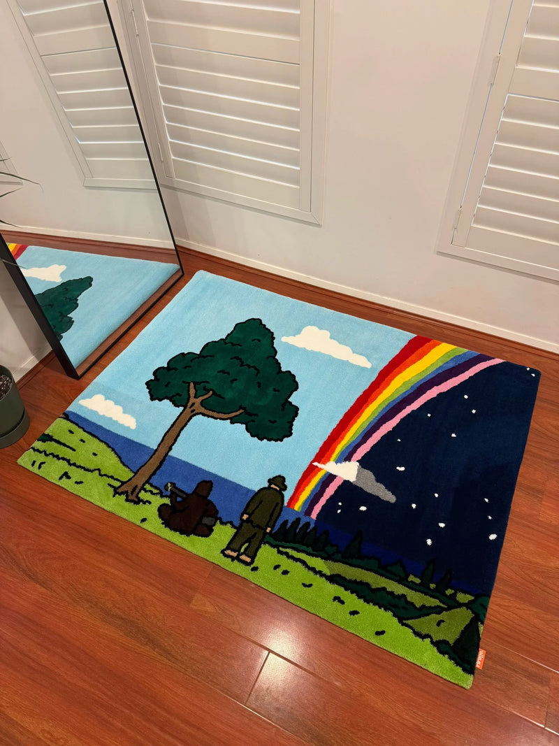 Handmade tufted rug with cartoon landscape featuring a tree, two figures, and a rainbow indoors