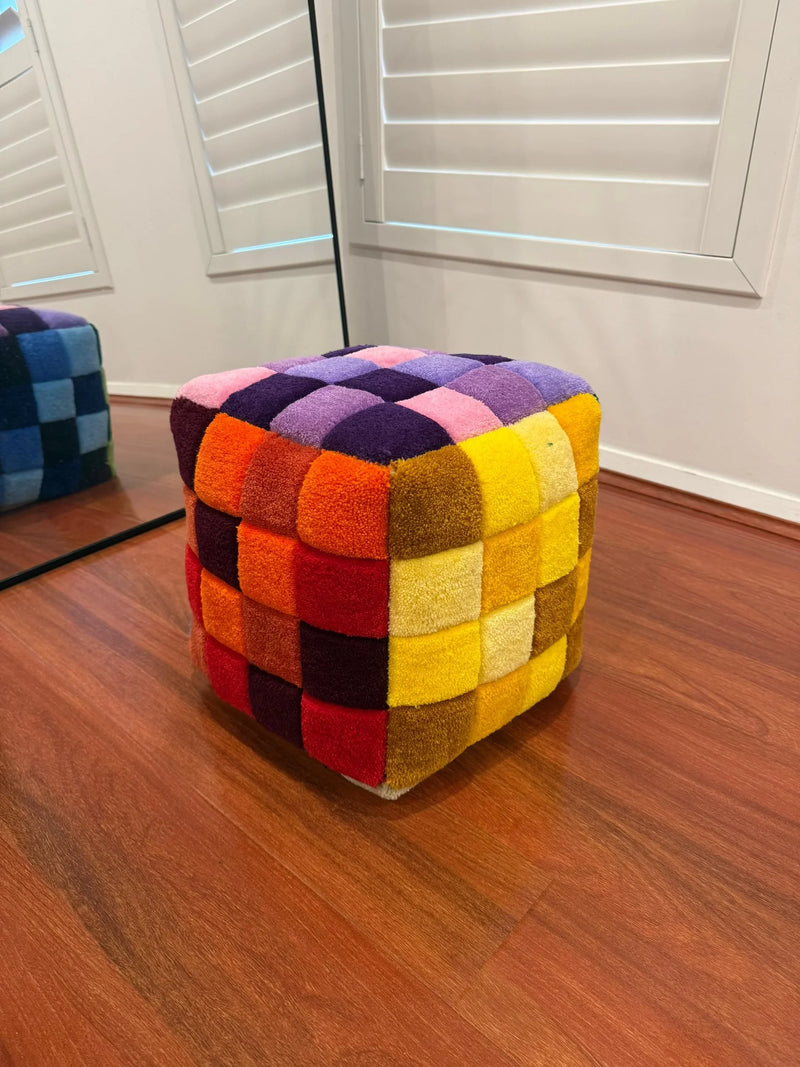 Handmade tufted cube ottoman with colorful checkered pattern on hardwood floor
