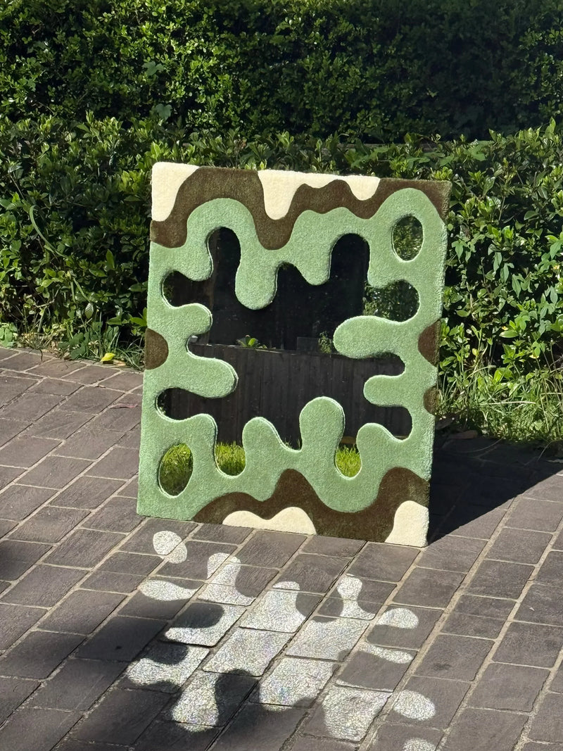 Handmade tufted mirror with green wavy pattern outdoors on stone pavement